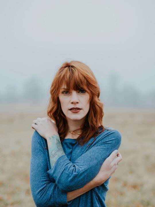 Nachdenkliche Frau mit roten Haaren in einem nebligen Feld – Symbol für Selbstreflexion, Transformation und persönliche Weiterentwicklung durch astrologisches Coaching bei Astroratgeber.com.